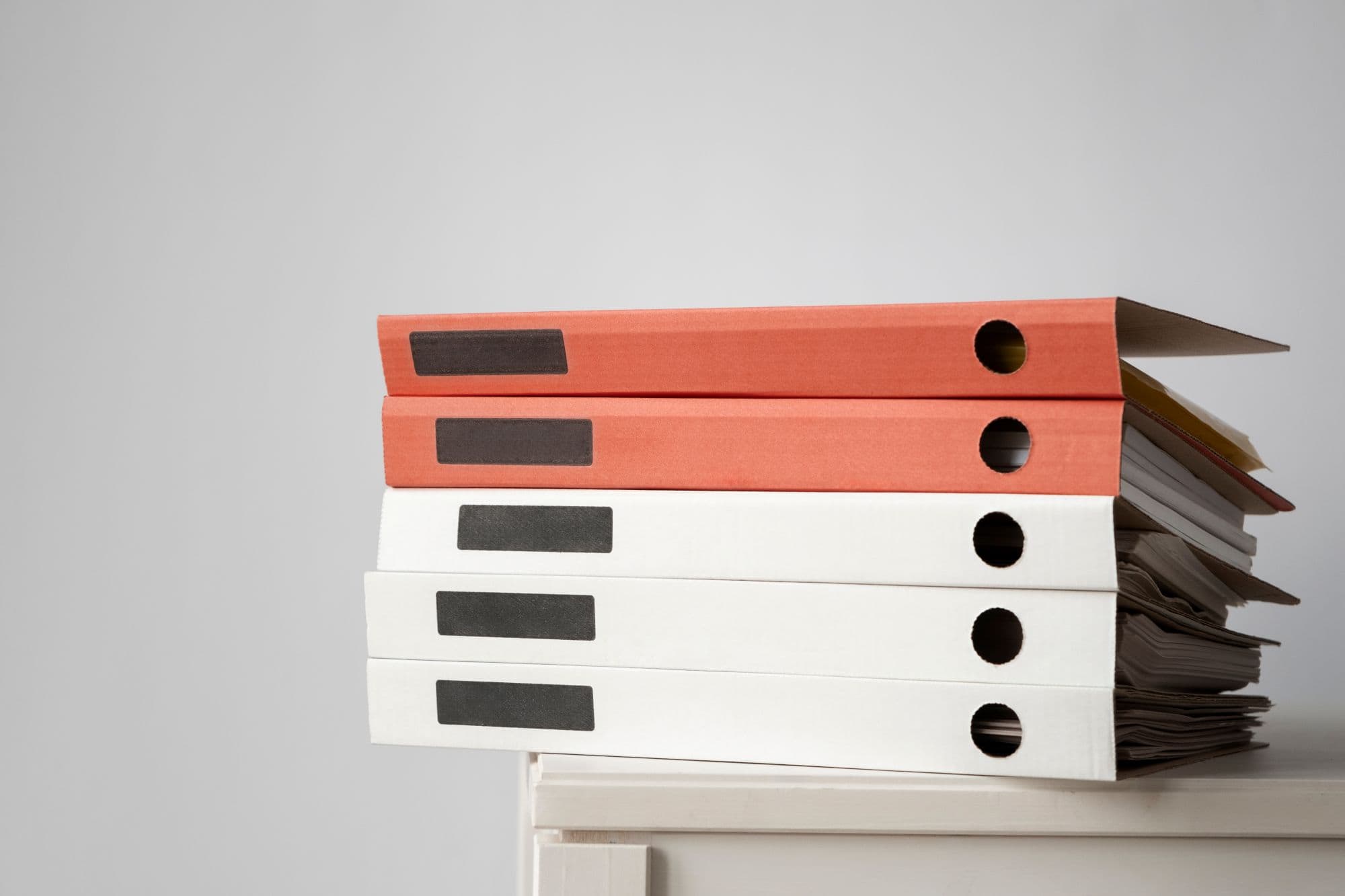 orange and white binders full of papers stacked on top of each other on top of a cabinet