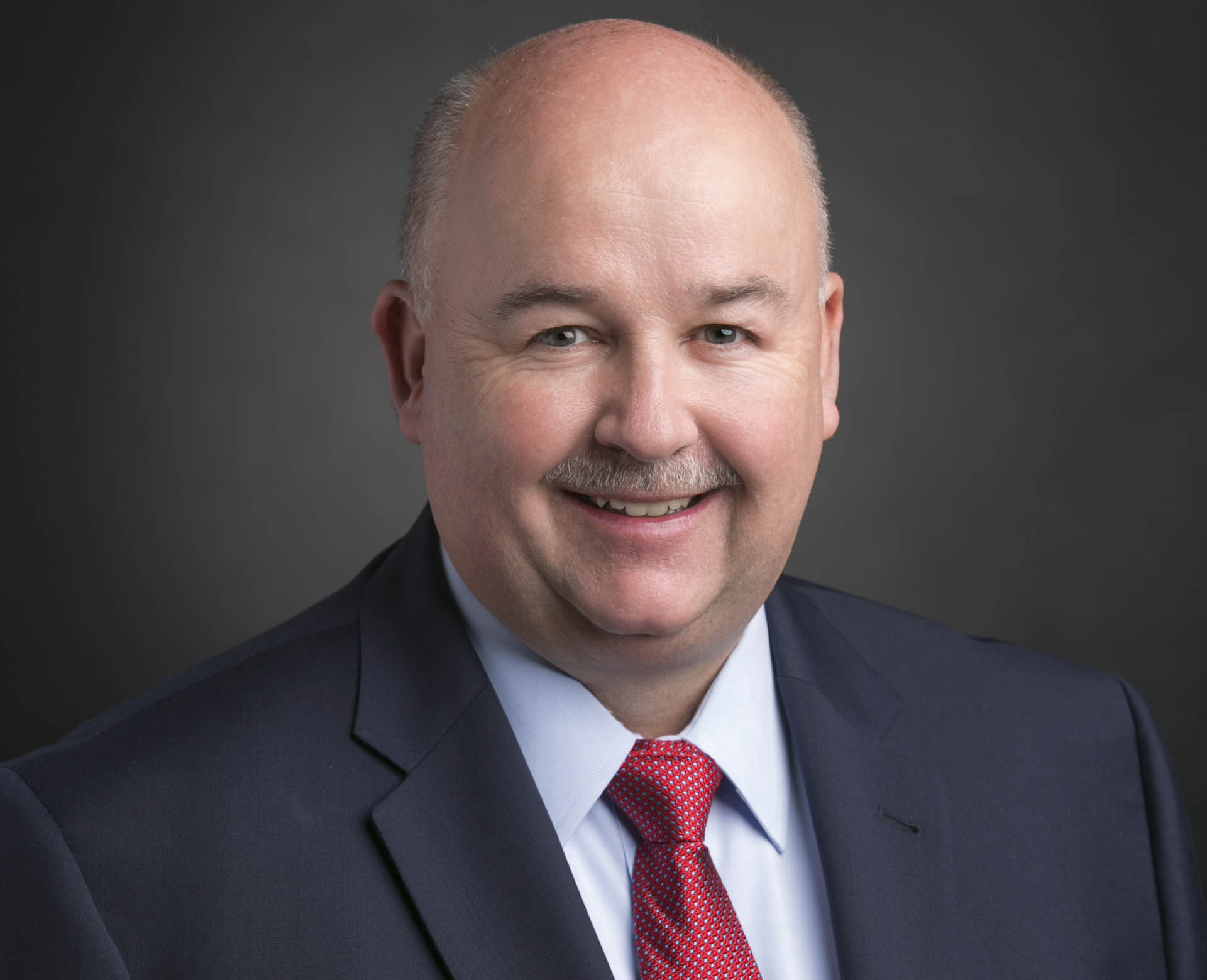 Man with mustache, red tie, and dark suit smiling for portrait photo